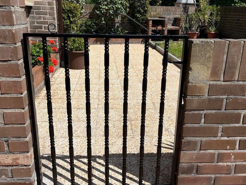 Puerta metálica de barrotes instalada en el acceso a un jardín